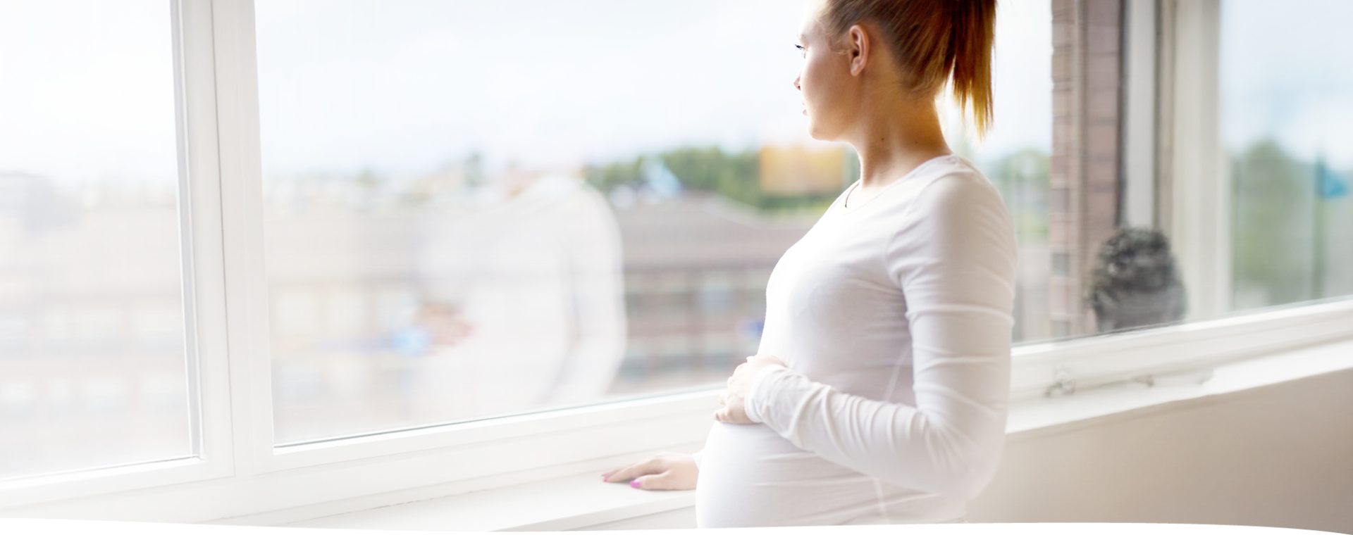 Schwangere Frau schaut aus Fenster